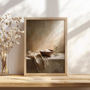 May include: A framed art print featuring a still life composition. A wooden bowl filled with white substance sits on a stone surface, accompanied by a sprig of leaves and draped fabric. The frame is light-colored wood.