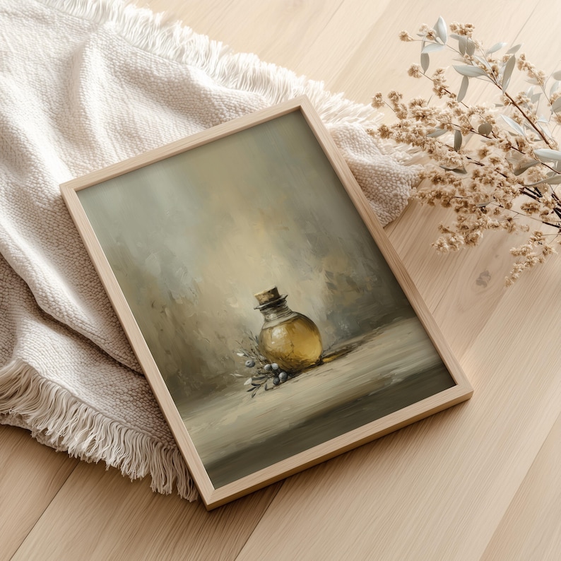 May include: A framed art print featuring a still life of a glass bottle with a cork stopper, olive branch, and a neutral color palette. The artwork is in a wooden frame and rests on a light-colored surface.