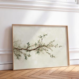 Può includere: Una stampa artistica rettangolare in una cornice di legno chiaro che raffigura un ramo d'albero orizzontale con piccole foglie verdi su uno sfondo color crema tenue e sfumato. L'opera presenta uno stile pittorico delicato con ombreggiature.