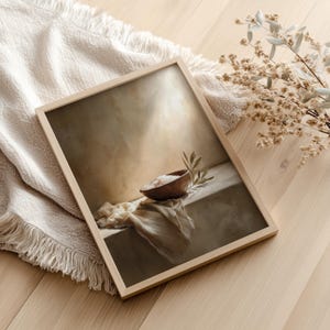 May include: A framed art print featuring a still life composition. The artwork depicts a wooden bowl filled with salt, a sprig of leaves, and a draped cloth. The frame is light-colored wood, and the overall color palette is neutral.