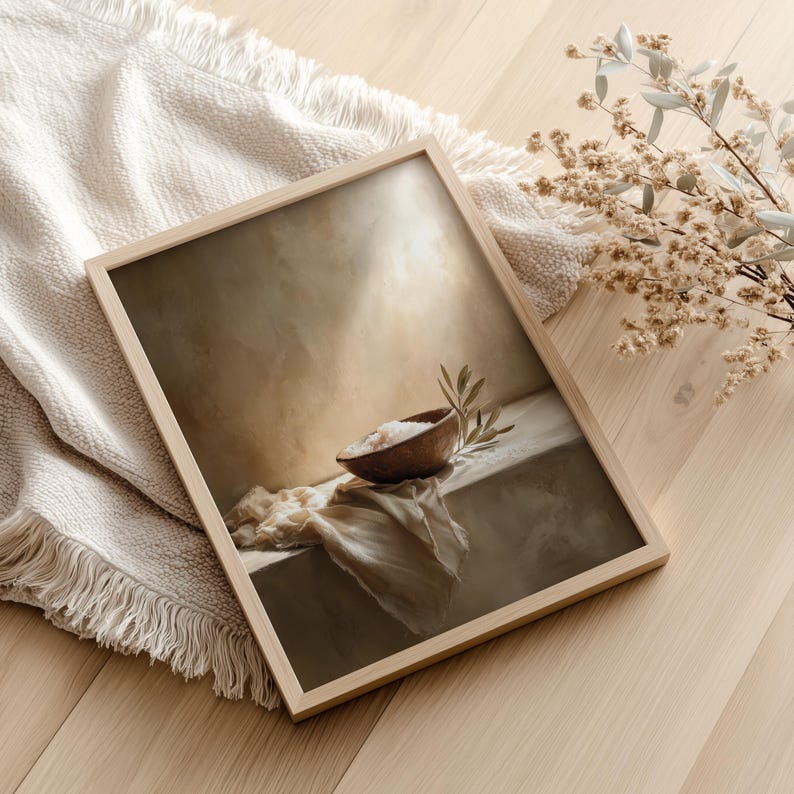 May include: A framed art print featuring a still life composition. The artwork depicts a wooden bowl filled with salt, a sprig of leaves, and a draped cloth. The frame is light-colored wood, and the overall color palette is neutral.