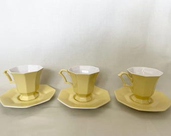 Könnte beinhalten: Drei gelbe Teetassen und Untertassen. Die Tassen haben ein geometrisches Design und weiße Innenräume. Die Untertassen sind achteckig. Das Set hat eine hellgelbe Farbe. Die Teetassen haben einen Henkel.