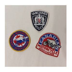 May include: Three embroidered patches. The first patch is blue, white and red with the text "Vancouver Police". The second patch is yellow, blue, white and red with the text "Canadian Motorcycle Association". The third patch is red, blue and white with the text "Canadian Motorcycle Association".