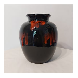 Puede incluir: Un jarrón de cerámica negro con esmalte naranja que gotea por los lados. El jarrón tiene un cuerpo redondeado y una abertura ancha.