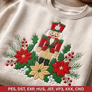 May include: A beige crewneck sweatshirt featuring an embroidered nutcracker figure in a red uniform, surrounded by red and gold poinsettia flowers, green holly leaves, pine needles, and white berries. The text PES, DST, EXP, HUS, JEF, VP3, XXX, CND.