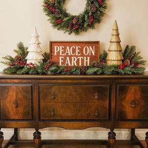 May include: A Christmas-themed display featuring a dark wood buffet adorned with festive decorations. A wreath hangs above, and a sign that reads "PEACE ON EARTH" is centered on the buffet. Decorative trees and greenery complete the holiday arrangement.