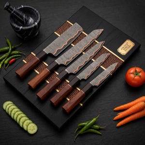 Può includere: Un set di cinque coltelli da cucina con lame in acciaio damasco e manici in legno scuro disposti su un tagliere in legno nero con etichetta dorata Ancient Forge Studio. Include un mortaio, cetriolo a fette, peperoncini verdi, carote e un pomodoro.