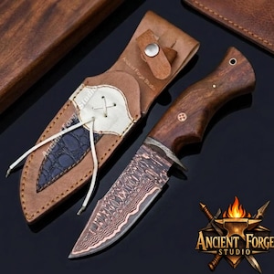 Peut inclure: Un couteau à lame fixe avec un manche en bois foncé et une lame en acier damas à motifs, accompagné d'un étui en cuir beige avec une incrustation texturée bleu foncé, un laçage blanc, un bouton-pression et le texte Ancient Forge Studio.