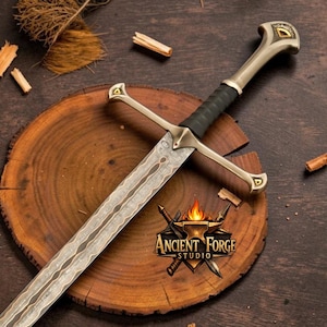May include: A metal sword with a patterned blade, a black grip, and a gold-toned crossguard and pommel. The pommel features a small triangular inlay. A logo with the text Ancient Forge Studio and a flame icon is visible on the blade.