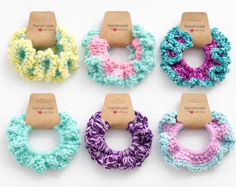 May include: Six handmade crochet scrunchies in various colors, including yellow, pink, teal, purple, and a mix. Each scrunchie has a brown tag that reads "Handmade with love". These hair accessories are perfect for adding a touch of color to any hairstyle.