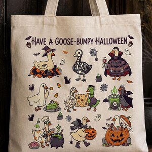 May include: A beige canvas tote bag featuring the text "HAVE A GOOSE-BUMPY HALLOWEEN" and a colorful illustration of various geese dressed in Halloween costumes, including a skeleton, a vampire, a mummy, a ghost, and a witch, alongside pumpkins.