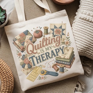 May include: Cream-colored tote bag with the text "Quilting is my Therapy" and illustrations of quilting tools and fabric. The design includes a pincushion, spools of thread, and a rotary cutter.