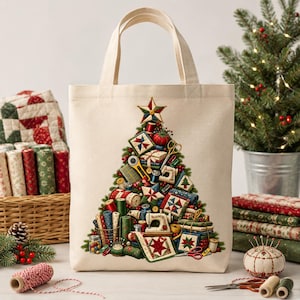 May include: A beige canvas tote bag featuring a central graphic of a Christmas tree constructed from sewing supplies, including fabric rolls, a sewing machine, scissors, and quilt blocks, topped with a star, all in festive red, green, and gold.