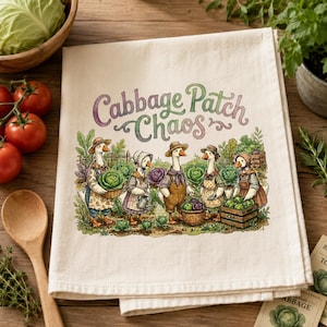 Könnte beinhalten: Ein cremefarbenes Küchentuch mit dem Text "Cabbage Patch Chaos" in einer verspielten Schriftart. Das Tuch zeigt eine Illustration von Gänsen, die als Bauern verkleidet sind und Kohl ernten. Die Gänse tragen Hüte und Schürzen und tragen Körbe und Kisten.