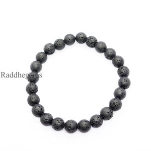 Puede incluir: Un brazalete de cuentas de piedra de lava negra. El brazalete está hecho de cuentas redondas y porosas ensartadas. Las cuentas son de color gris oscuro y tienen una textura rugosa. El texto "Raddhegems" es visible.