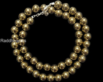 May include: A double strand necklace featuring polished, golden-colored beads. The beads are strung together with a silver-colored clasp. The necklace is displayed against a black background, highlighting the jewelry's color and shine.