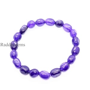 May include: A bracelet made of polished, oval-shaped purple gemstones. The beads are strung together to form a circular shape. The text "Raddhegems" is visible on the left side of the image.