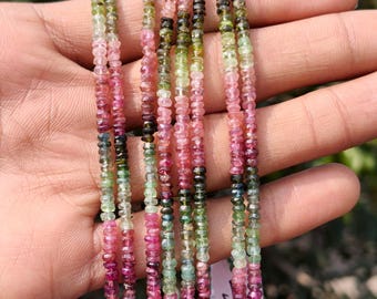 May include: Strands of colorful tourmaline beads in shades of pink, green, and black. The beads are small and strung together, creating a vibrant and natural gemstone jewelry piece. The beads are held in a hand.