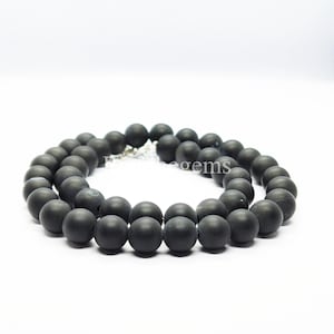 May include: A necklace featuring matte black beads. The beads are spherical and consistent in size, connected by a silver-toned clasp. The necklace is presented against a white backdrop.