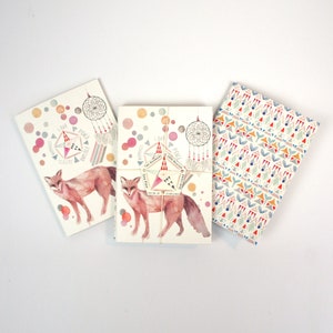 May include: Three watercolor notepads with a fox illustration and a dreamcatcher design. The notepads have a white background with pink, orange, and blue accents. The text on the notepads reads "Love, Peace, Happiness, Gratitude, Two Worlds, One Planet, Give First, Feel Love, Dream Big, Be Kind, Be Present, Be You".