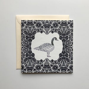 May include: A black and white card with a stylized illustration of a goose in a black and white floral frame.