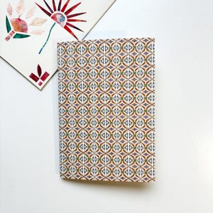 Peut inclure: Un petit carnet avec une couverture à motif géométrique brun, vert et blanc.