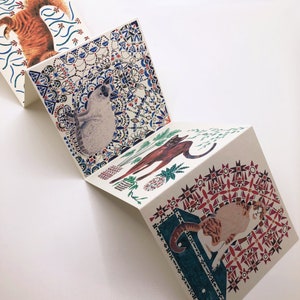May include: A set of four folded cards with colorful patterned designs featuring cats and plants. The cards are folded in half and have a white background with blue, red, and green accents.