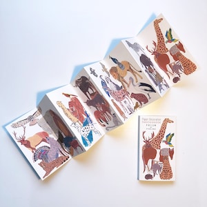 Può includere: Un libro di decorazione in carta con il tema del prisma della quiete. Il libro è aperto per mostrare le diverse illustrazioni di animali, tra cui una giraffa, una zebra, un leone, un elefante e altro ancora. Il libro è intitolato "Paper Decoration Prism of Stillness".