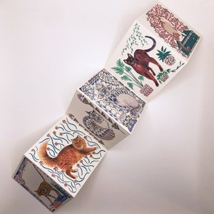 May include: A folded card with a colorful design featuring cats and flowers. Each panel of the card has a different cat illustration with a unique background.