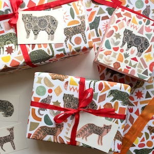 May include: Three gift boxes wrapped in white paper with a colourful geometric pattern featuring animals. The boxes are tied with red ribbon and have gift tags with animal illustrations.