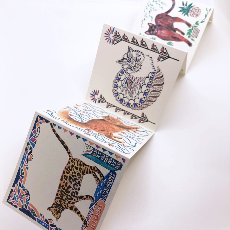 May include: A folded card with a colorful, patterned design featuring four different cats. The card has the text "ILLUSIONS", "ARTHRLOVE", "EMOHOME", and "SPIRIT" on it.