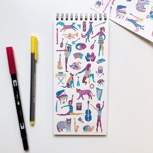 May include: A white spiral bound notebook with a colorful illustration of a circus theme. The illustration includes animals, musical instruments, and people performing. The notebook is perfect for taking notes, sketching, or journaling.