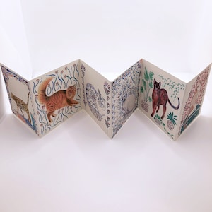 May include: A folded paper book with colorful illustrations of cats on each page. The cats are depicted in various poses and surrounded by floral and geometric patterns.