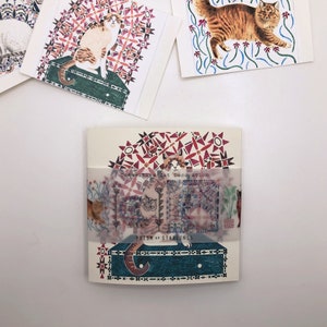 May include: A set of four illustrated cards featuring cats in a geometric pattern. The cards are printed on white cardstock and have a red, blue, and green color scheme. The text on the cards reads "Constellation Cat Decoration" and "Prism of Starlings".
