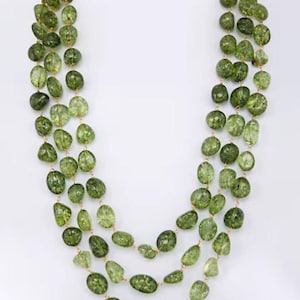 May include: A three-strand necklace with olive-green, irregularly shaped beads. The beads are strung on delicate gold-coloured chains. The necklace is set against a plain white background, highlighting the natural colour and texture of the gemstones.