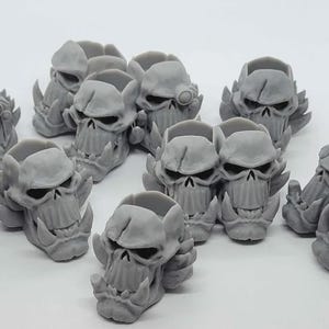 May include: A collection of gray, skull-shaped figurines with detailed features, including prominent teeth and eye sockets. The skulls have a rough texture and are arranged in a group, suggesting a thematic or decorative purpose.
