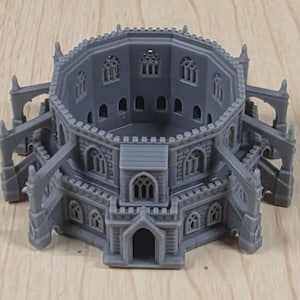 Puede incluir: Modelo gris impreso en 3D de un edificio de estilo medieval con pasarelas arqueadas y múltiples ventanas arqueadas. La estructura tiene un diseño circular con una fachada detallada y un techo.