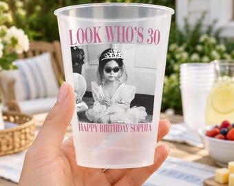 May include: A translucent plastic party cup featuring a black and white photograph of a child wearing a tiara and sunglasses. The text "LOOK WHO'S 30" is printed in pink above the photo, and "HAPPY BIRTHDAY SOPHIA" is printed in pink below the photo.