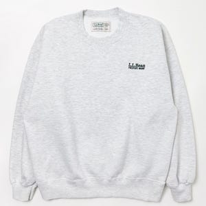 May include: A light gray sweatshirt with the text "L.L.Bean Freeport, Maine" in dark green. The sweatshirt has a crew neck, long sleeves, and ribbed cuffs and hem. A small tag is visible near the neckline.