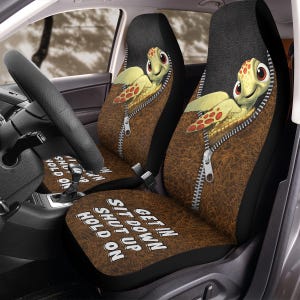 May include: Car seat covers featuring a cartoon turtle design. The turtle is peeking out of a brown, textured pocket with a zipper. The seat covers have the phrases "GET IN SIT DOWN SHUT UP HOLD ON" printed on them.