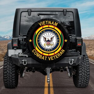 May include: A black spare tire cover mounted on the back of a vehicle, featuring the United States Navy emblem in the center with the text VIETNAM COMBAT VETERAN arched around the top and bottom in yellow capital letters on a black background.