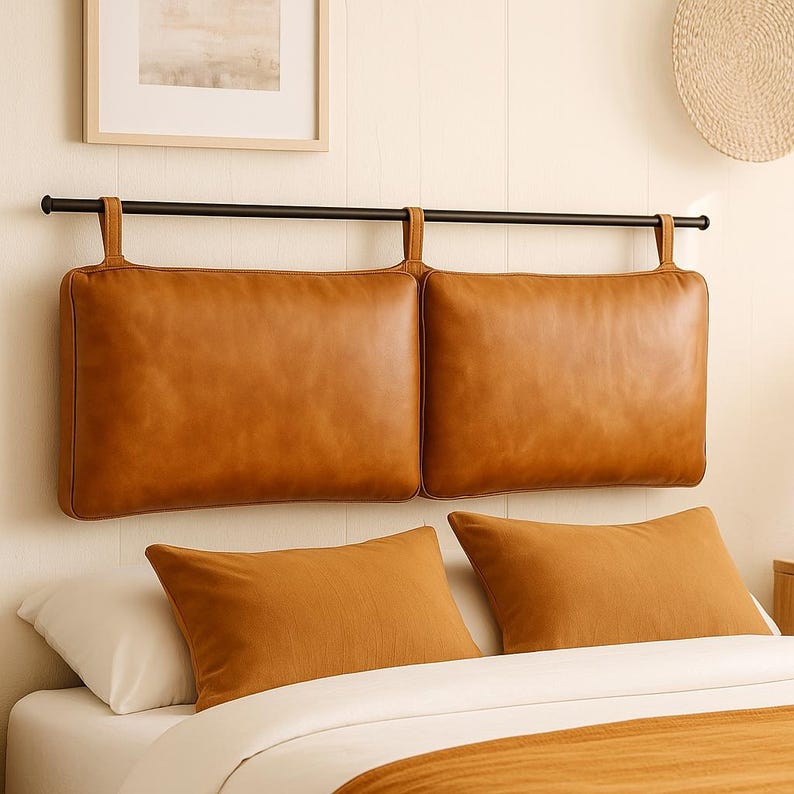 May include: A headboard with two rectangular, tan leather cushions suspended from a black metal bar. Two matching tan pillows rest on the bed below. The bed is made with white sheets and a tan blanket.