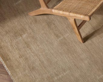 May include: A neutral-toned, woven area rug with a textured surface. The rug is paired with a wooden chair with a woven seat and back. The chair has a light brown finish and a minimalist design. The rug's color is a light tan.