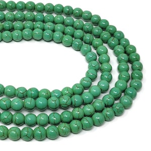 May include: A strand of turquoise beads, each bead is round and has a green color with brown veins. The beads are arranged in a circular pattern.