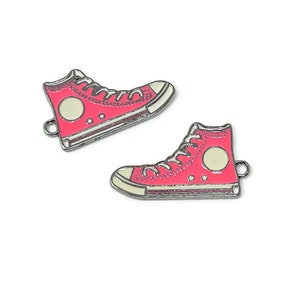 May include: Two pink enamel metal charms shaped like high-top sneakers with white laces and a white circle on the side.