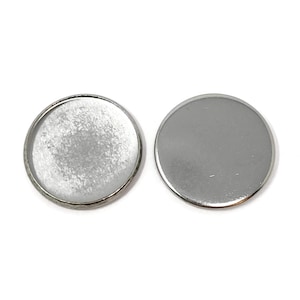 May include: Two silver-colored, round bezel trays for jewelry making. One tray has a textured interior, and the other is a smooth, solid circle. Both are set against a white background.