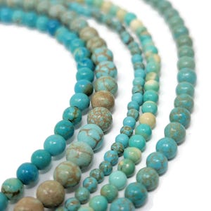 May include: Four strands of round turquoise beads arranged in a curved pattern. The beads vary in size and feature natural veining in shades of bright blue, teal, and earthy brown. Each strand displays a smooth, polished finish with consistent spherical shapes.