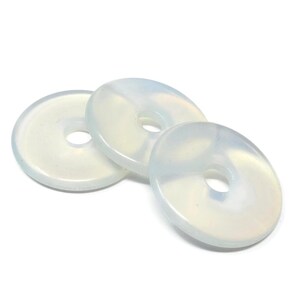 May include: Three white opal donut shaped beads with a hole in the center. The beads are smooth and have a slight iridescent sheen.