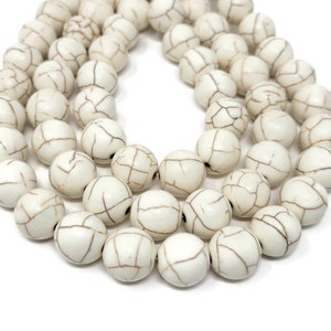 May include: A strand of white howlite beads with brown veining. The beads are round and smooth, and they are strung on a white cord.