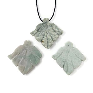 May include: Three leaf-shaped pendants carved from pale green stone. One pendant is suspended from a thin black cord, while the other two are positioned below it. Each piece features carved vein details and a smooth, polished surface texture.